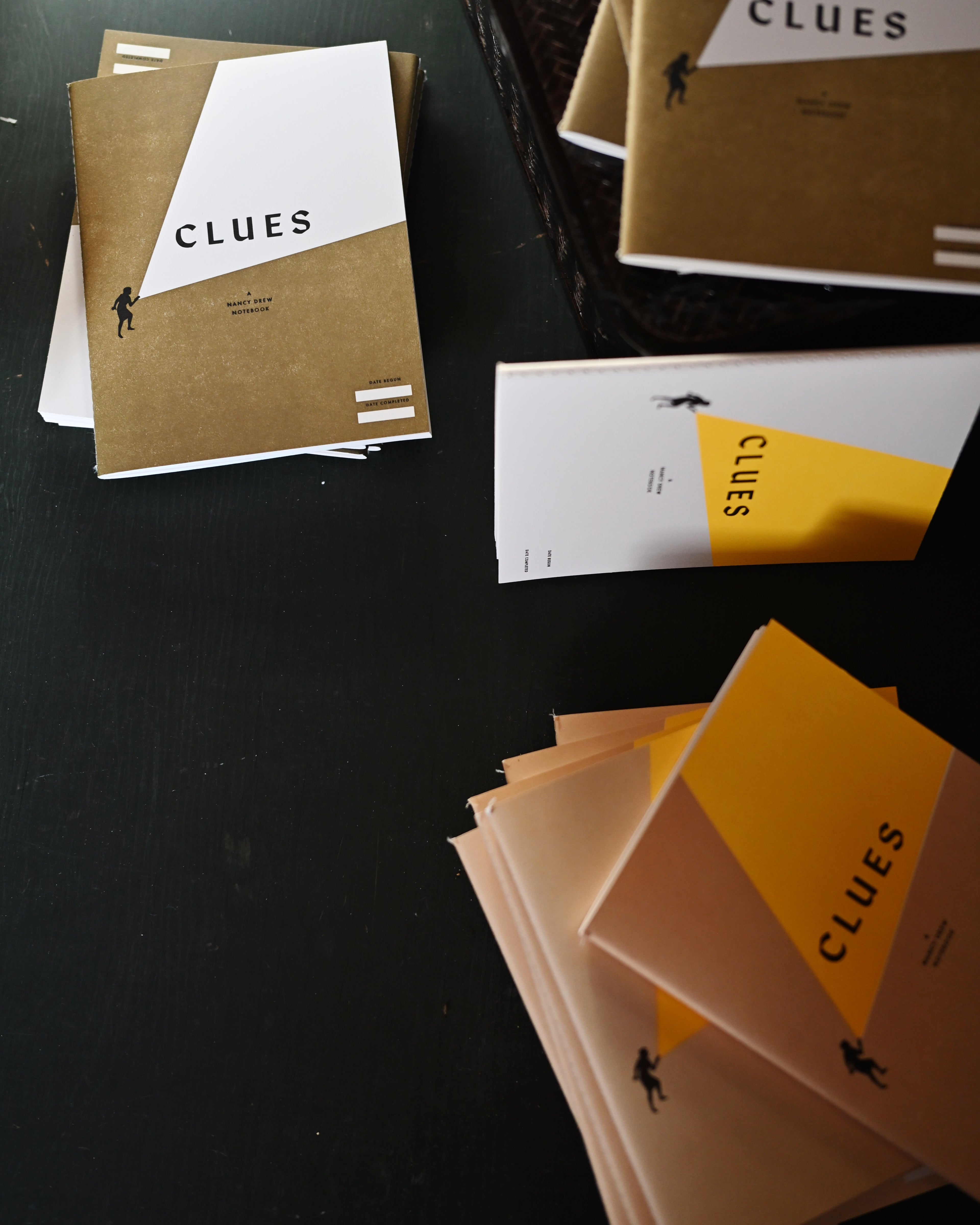 3 different colours of letterpress clues nancy drew notebooks displayed at jaunty angles against vintage ping pong table background